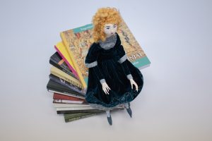 Rankų darbo medžiaginė lėlė "pasodinta" ant knygų krūvos.
