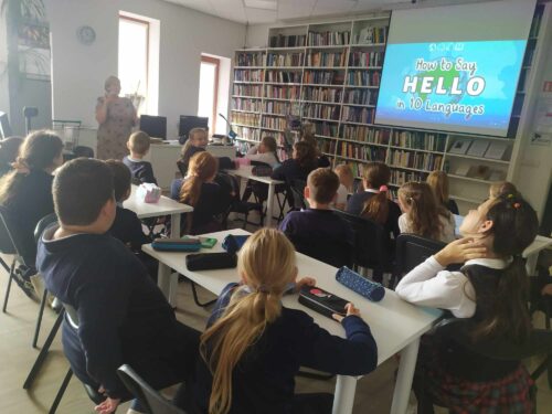 Daug vaikų sėdi prie stalų bibliotekoje.