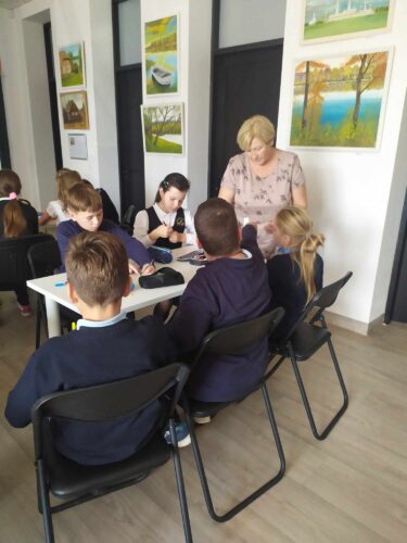 Daug vaikų sėdi prie stalų bibliotekoje.