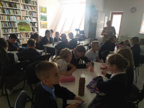 Daug vaikų sėdi prie stalų bibliotekoje.