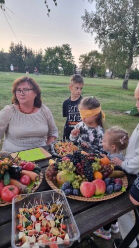 Užrištomis akimis, ragaudami bando atspėti vaisių ar daržovę. Prie stalo 4 vaikai ir suaugus moteris su akiniais. Vynuogės, obuoliai, slyvos, mangas, pomidorai, morkos, agurkai, baklažanas