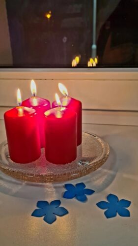 Uždegtos keturios raudonos žvakės. Šalia guli trys mėlyni neužmirštuolių žiedai.