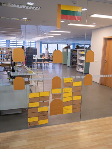 Bibliotekoje ant stiklo suklijuoti spalvoti lapukai. Panašu į pilį.