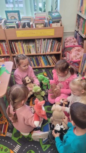 Vaikai bibliotekoje žaidžia su pliušiniais žaislais.